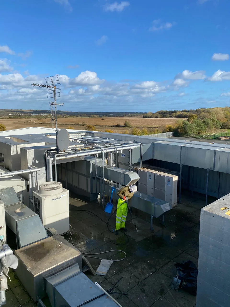 Operative carrying out commercial roof cleaning around roof-mounted plant